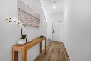 A hallway with a wooden console table, a potted plant, and a painting on the wall. - Lost Bay Townhome 4239 (Orange Beach)
