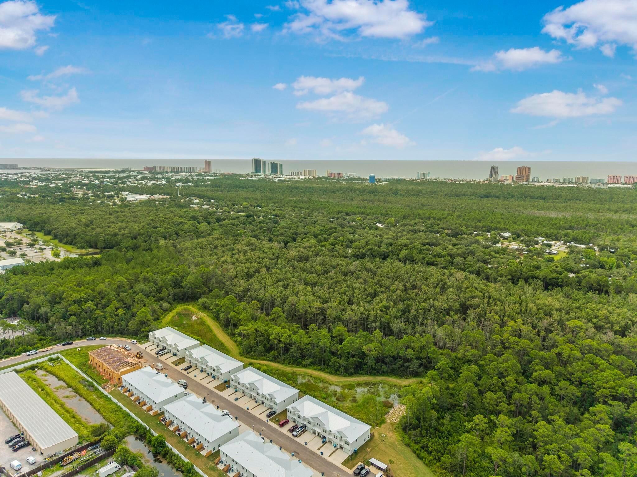 An aerial view of a residential area with a large building complex, surrounded by dense greenery and a coastline in the background.
