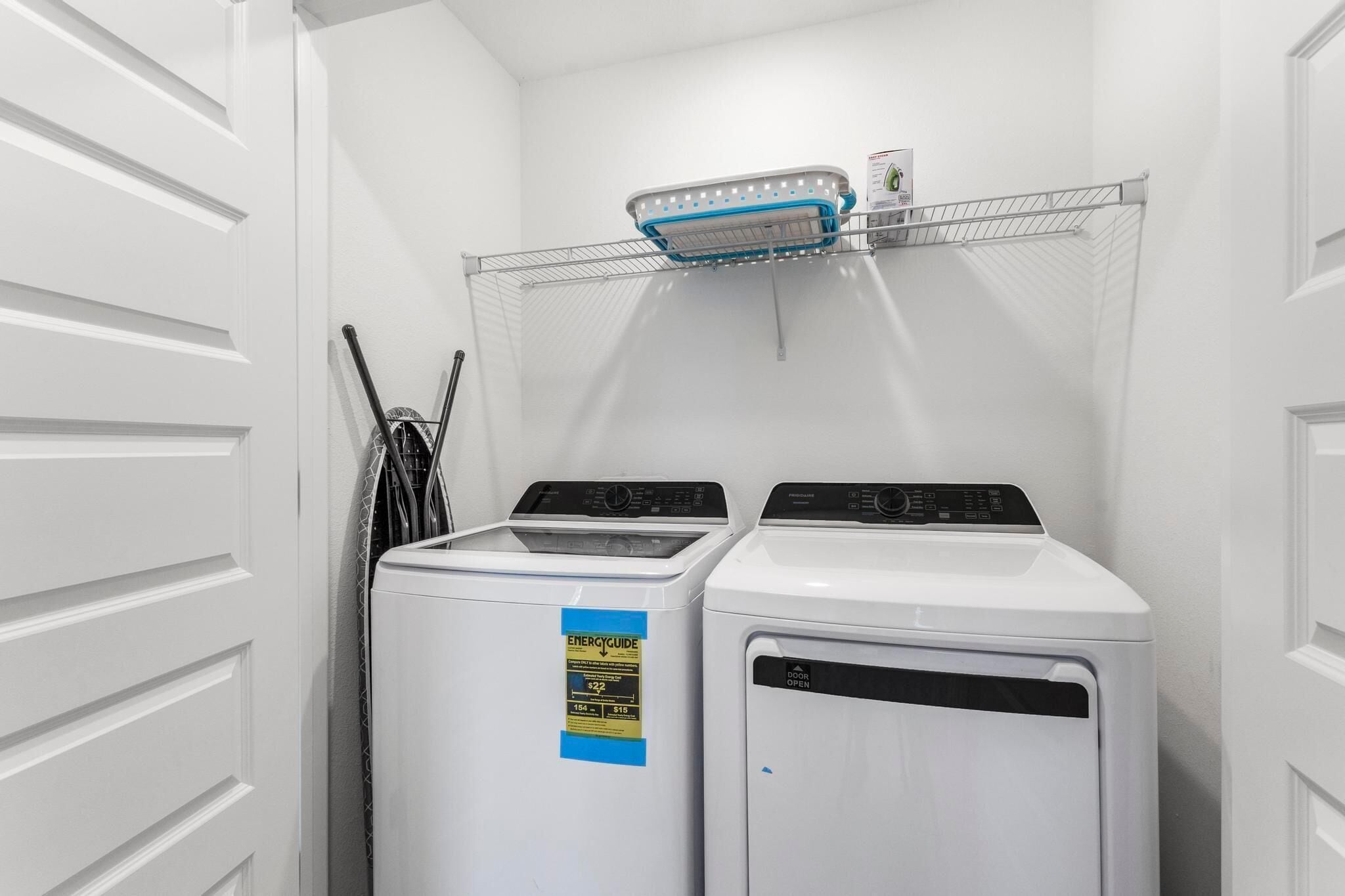 A laundry room with two front-loading washing machines and a drying rack above them.