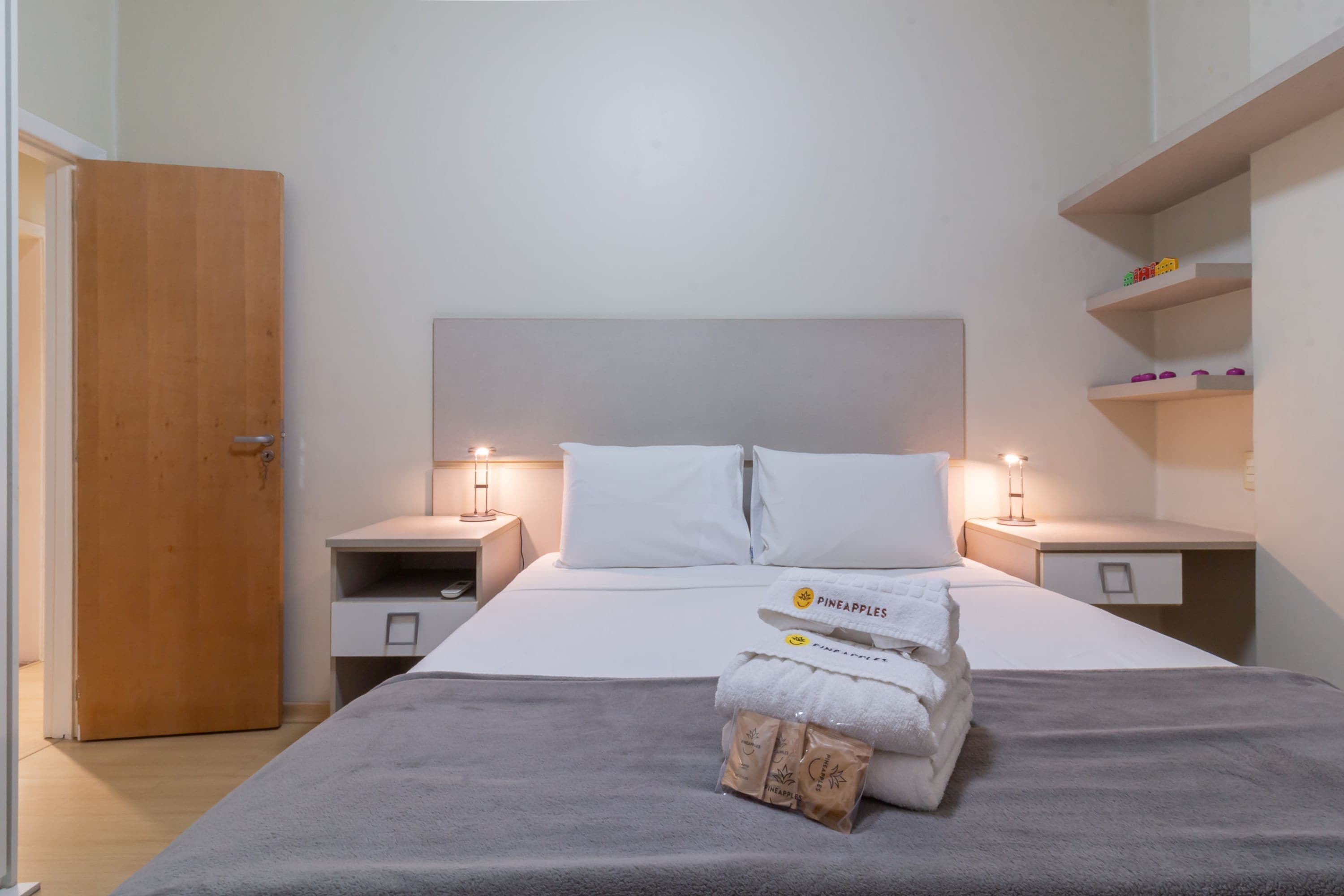 Een hotelkamer met een bed, twee nachtkastjes, een plank met spullen en een houten deur.