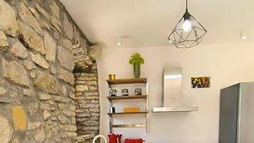 A kitchen with a stone wall, a modern pendant light, and a stainless steel refrigerator.