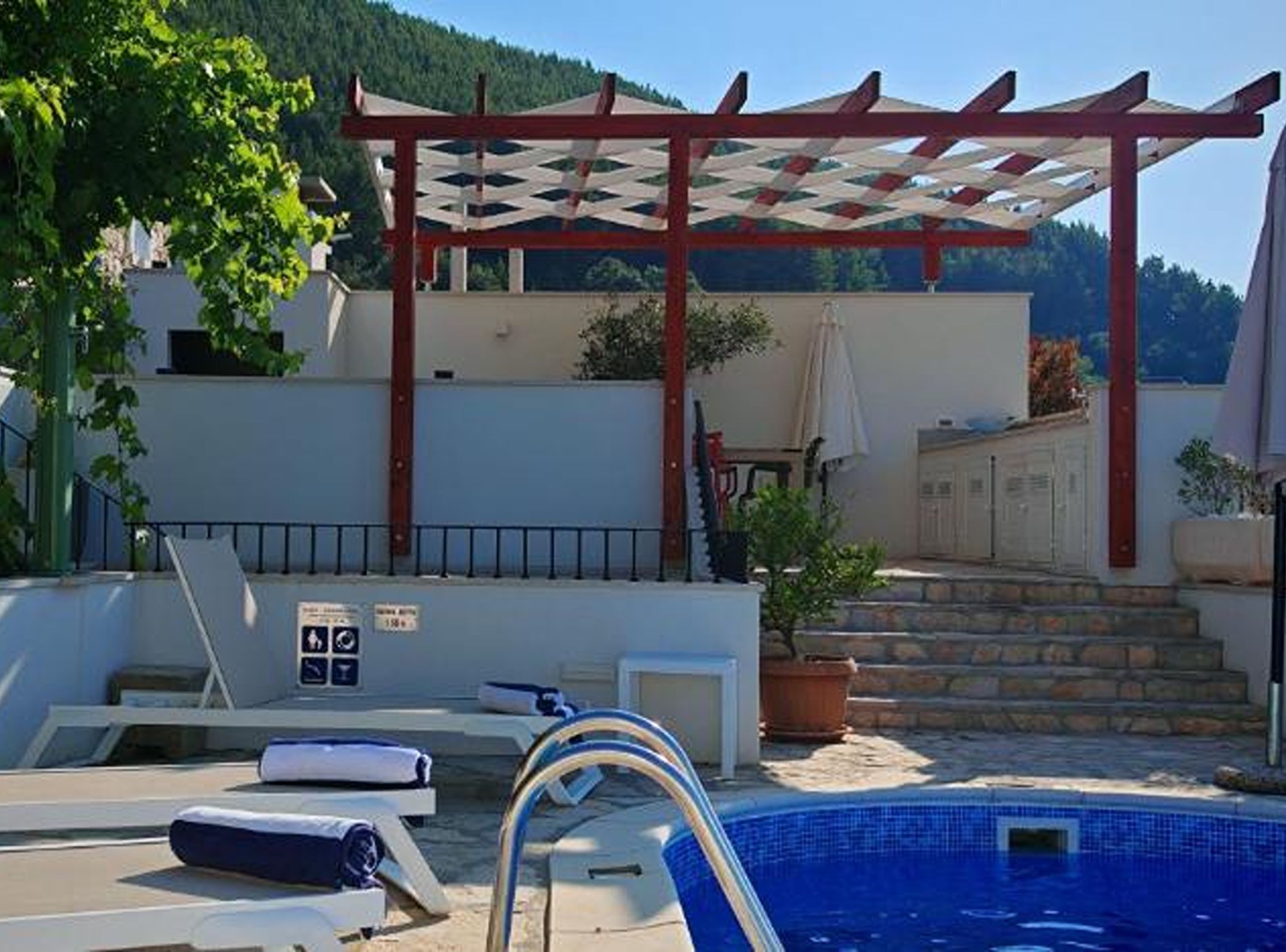 Ein Poolbereich mit Liegestühlen, einer Pergola und einer Treppe zu einem Gebäude.