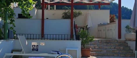 Un área de piscina con sillones, una pérgola y una escalera que lleva a un edificio.