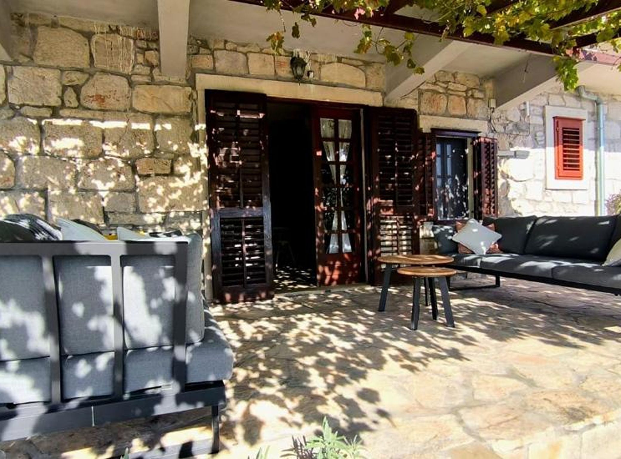 A stone patio with a sofa and two tables, a stone wall, and a door with shutters.