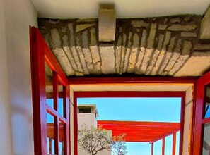 An interior corridor with a stone ceiling, red-framed windows, and a view of a building outside. - Panoramic View Relax Villa Smoquizza (Smokvica)