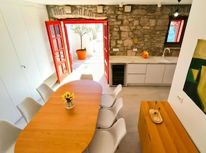A modern kitchen with a stone wall, a wooden dining table with chairs, and a red-framed door leading outside. - Panoramic View Relax Villa Smoquizza (Smokvica)