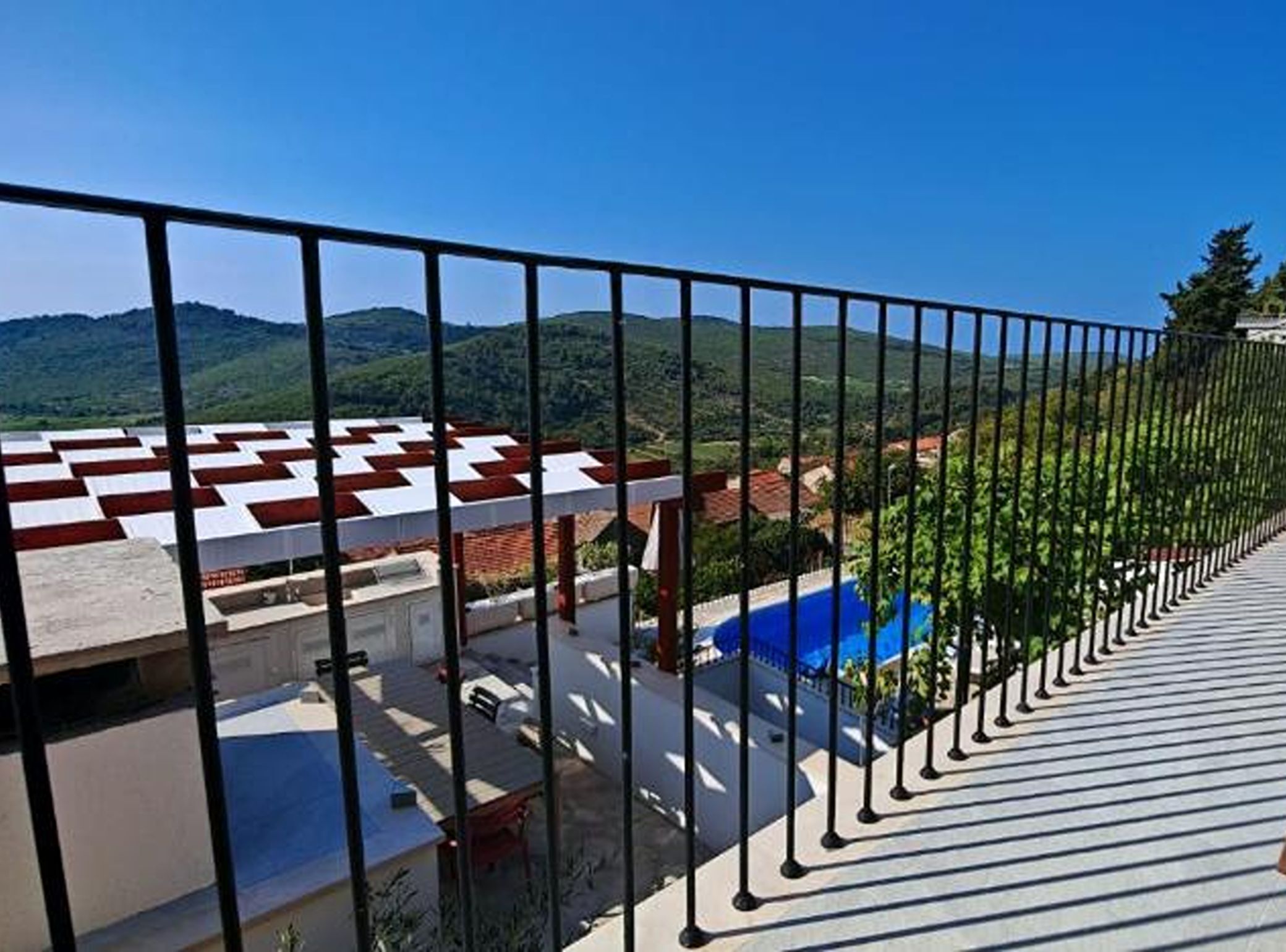 A balcony with a metal railing overlooking a pool and a mountainous landscape.