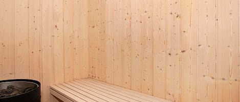 A sauna room with wooden walls, a bench, and a trash bin.