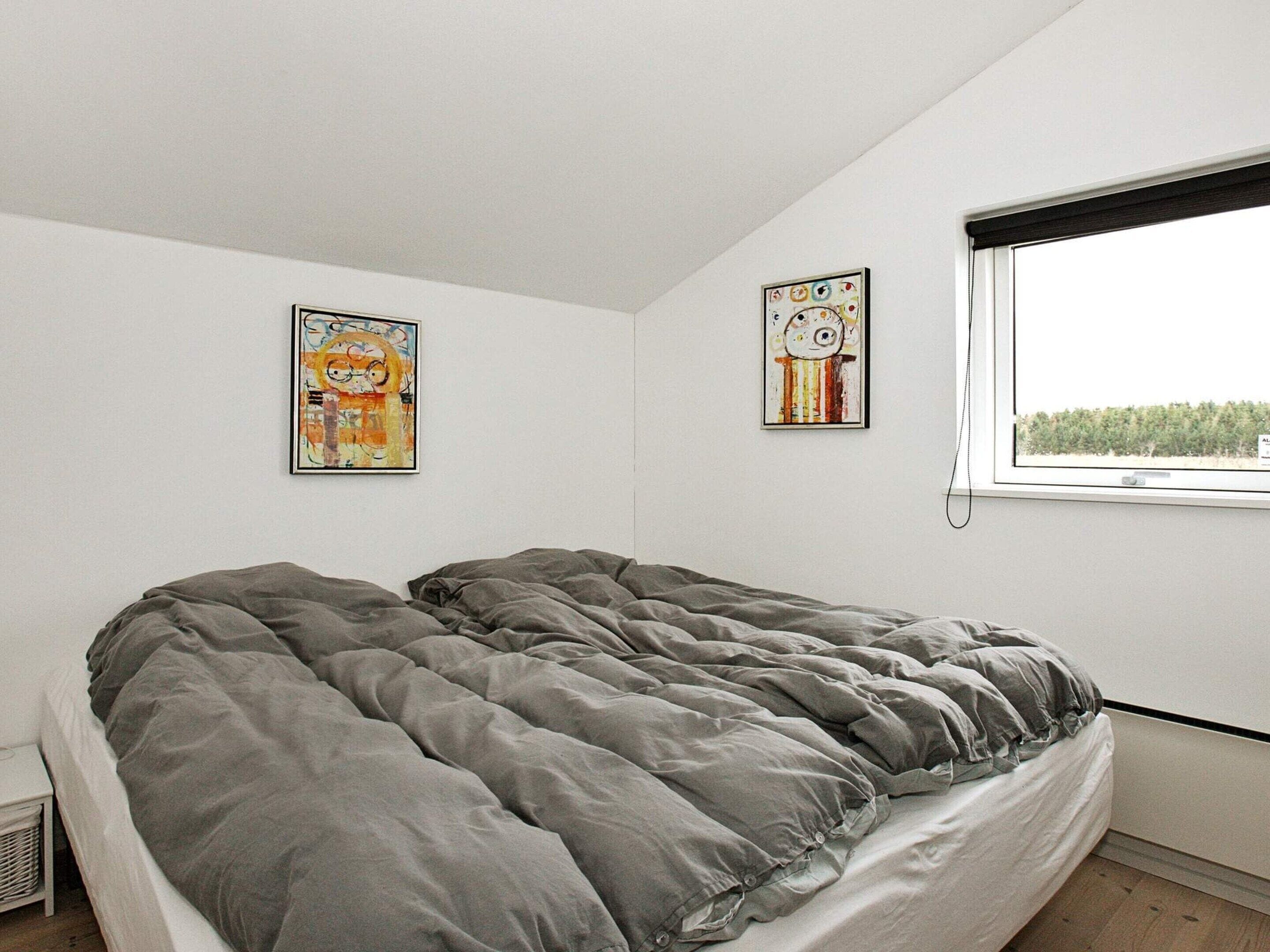 Un dormitorio con una cama, dos obras de arte colgadas en la pared, una ventana con vistas y una mesita de noche pequeña.
