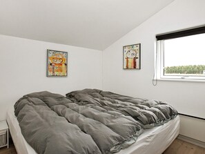 Ein Schlafzimmer mit einem Bett, zwei an der Wand befestigten Kunstwerken, einem Fenster mit Blick und einem kleinen Nachttisch.