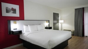 A hotel room with a large bed, bedside tables with lamps, a wall-mounted picture, a door, and a window with curtains. - Pet-Friendly Tulsa-Area Stay with Free Breakfast & Parking (Broken Arrow)