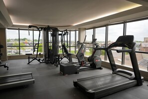 A gym with various exercise equipment, large windows, and a view of the outside.