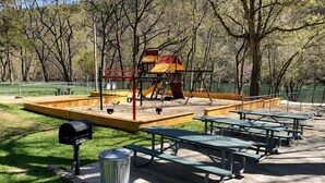 A playground with swings and a slide, surrounded by picnic tables and a trash can. - Welcome to Royale Relaxation at Pointe Royale in Branson, Missouri! (Branson)