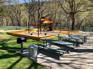 A playground with swings and a slide, surrounded by picnic tables and a trash can. - Welcome to Royale Relaxation at Pointe Royale in Branson, Missouri! (Branson)