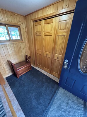 A room with wooden panel walls, a blue door, a bench, and a window.
