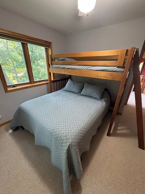 A bunk bed with a headboard, a window with a view of trees, and a carpeted floor.