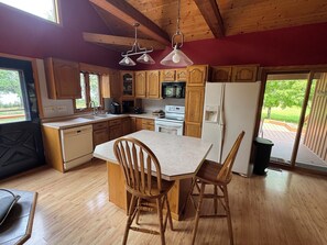 A kitchen with wooden cabinets, a central island with chairs, a refrigerator, and a microwave.
