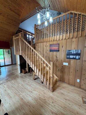 A wooden staircase with a railing leading to a balcony, a chandelier, and a fireplace.