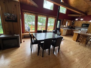 A spacious kitchen with wooden cabinets, a dining area with a large table and chairs, and large windows offering a view of the outdoors. - Quiet Northwoods Retreat - Sunset & Lake Views, King Suite, Laundry, Fast Wi-Fi (Bemidji)