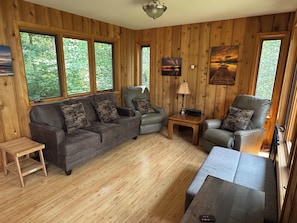 Una habitación con paneles de madera, un sofá, dos sillones, una mesita y una lámpara.