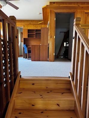 A wooden staircase leading to a room with a desk and chair, a ceiling fan, and a view of a staircase in the background. - Quiet Northwoods Retreat - Sunset & Lake Views, King Suite, Laundry, Fast Wi-Fi (Bemidji)