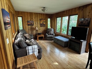 A cozy living room with a sofa, armchair, ottoman, and a television. - Quiet Northwoods Retreat - Sunset & Lake Views, King Suite, Laundry, Fast Wi-Fi (Bemidji)