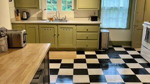 Une cuisine avec un carrelage à motifs, des placards verts, un évier et une fenêtre donnant sur un paysage verdoyant.