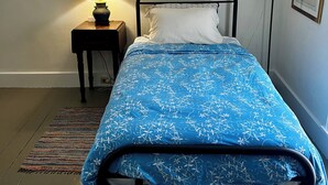 Un lit simple avec une couvre-lit à motifs floraux bleus, une table de chevet avec une lampe et un tableau encadré au mur.