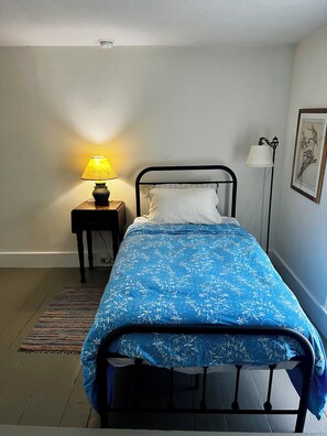 Un lit simple avec une couvre-lit à motifs floraux bleus, une table de chevet avec une lampe et un tableau encadré au mur.
