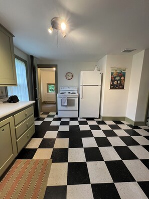A kitchen with a black and white checkered floor, a stove, a refrigerator, and a clock on the wall.