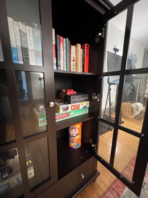 A bookshelf with various books and board games, a window with a view of a room, and a door with a handle.