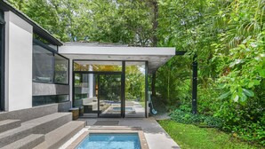 A modern outdoor pool area with a glass-enclosed patio, steps leading to a pool, and lush greenery surrounding the space. - Family Home with Private Pool – 5 Min drive to the Beach (Tamarindo)