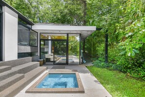Ein moderner Poolbereich im Freien mit einer verglasten Terrasse, Treppen zum Pool und üppiger Bepflanzung rundherum.