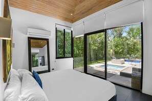 Ein modernes Schlafzimmer mit einem großen Bett, Blick auf einen Swimmingpool und einer Holzzieldecke.