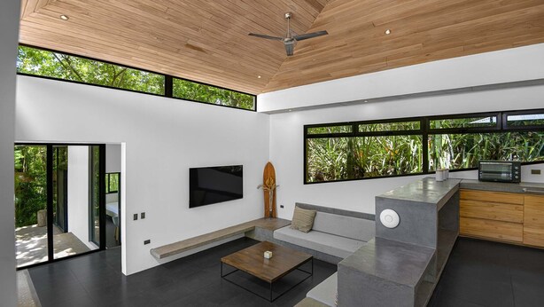 A modern interior with a flat-screen TV, a wooden ceiling, and large windows offering a view of greenery. - Family Home with Private Pool – 5 Min drive to the Beach (Tamarindo)