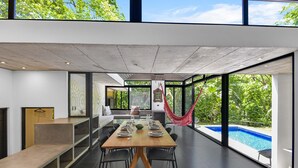 A modern dining area with a wooden table and chairs, large windows, and a view of a swimming pool. - Family Home with Private Pool – 5 Min drive to the Beach (Tamarindo)