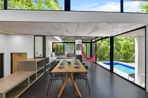 Ein moderner Essbereich mit Holztisch und -stühlen, großen Fenstern und Blick auf einen Swimmingpool.