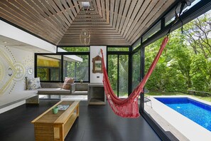 Un salon moderne avec un hamac, une piscine et de grandes fenêtres donnant sur un espace verdoyant.
