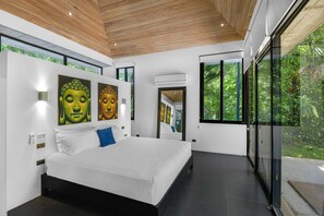 Une chambre moderne avec un grand lit, un plafond en bois et de grandes fenêtres donnant sur un paysage verdoyant.