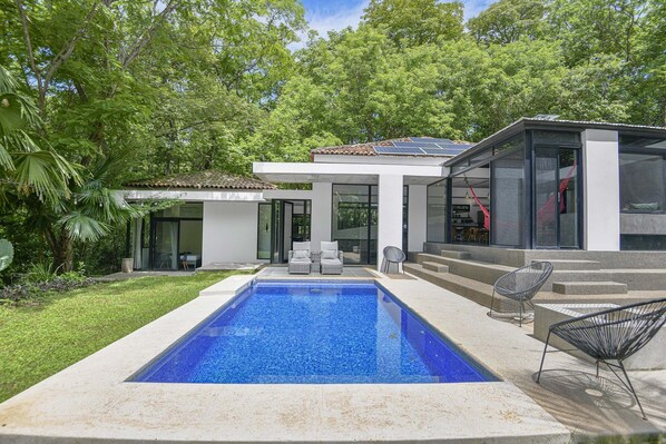 Une maison moderne dotée d’une piscine, d’un espace salon extérieur et d’un jardin.