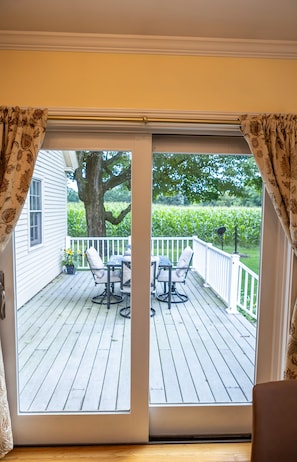 A view through a sliding glass door onto a wooden deck with outdoor furniture, a tree, and a hedge. - Beautiful, Charming and Private house close to EVERYTHING. A/C and Fast Wifi (Orford)
