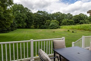 A deck with a table and chairs, overlooking a well-maintained lawn and a cornfield.