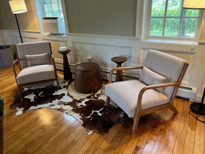 A room with two chairs, a round ottoman, a small table, and a cowhide rug.