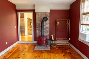 Une pièce avec une cheminée en briques rouges, un plancher en bois et une fenêtre avec des stores.