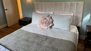Quarto com cama, mesa de cabeceira, luminária na parede e porta.