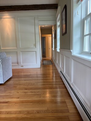 Ein Flur mit Holzdielen, weißen Wänden und einer Tür zu einem anderen Zimmer.