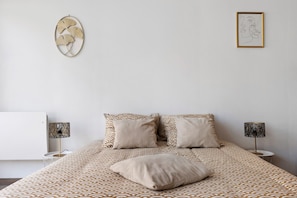 A bedroom with a patterned bedspread, two pillows, a bedside table with a lamp, and a wall art piece.