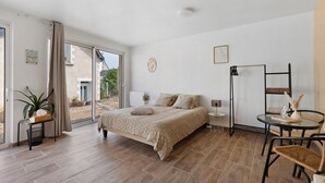 A bedroom with a bed, a bedside table, a chair, a small table, and a view through a sliding door to an outdoor area.