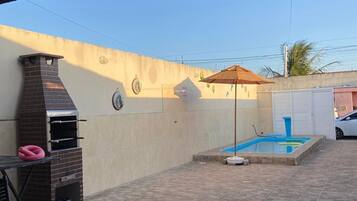 Un patio couvert comprenant un barbecue, une petite piscine et une table avec des chaises.