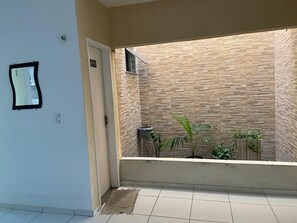 A small, enclosed outdoor area with tiled flooring, a door, a wall with a textured pattern, and potted plants.